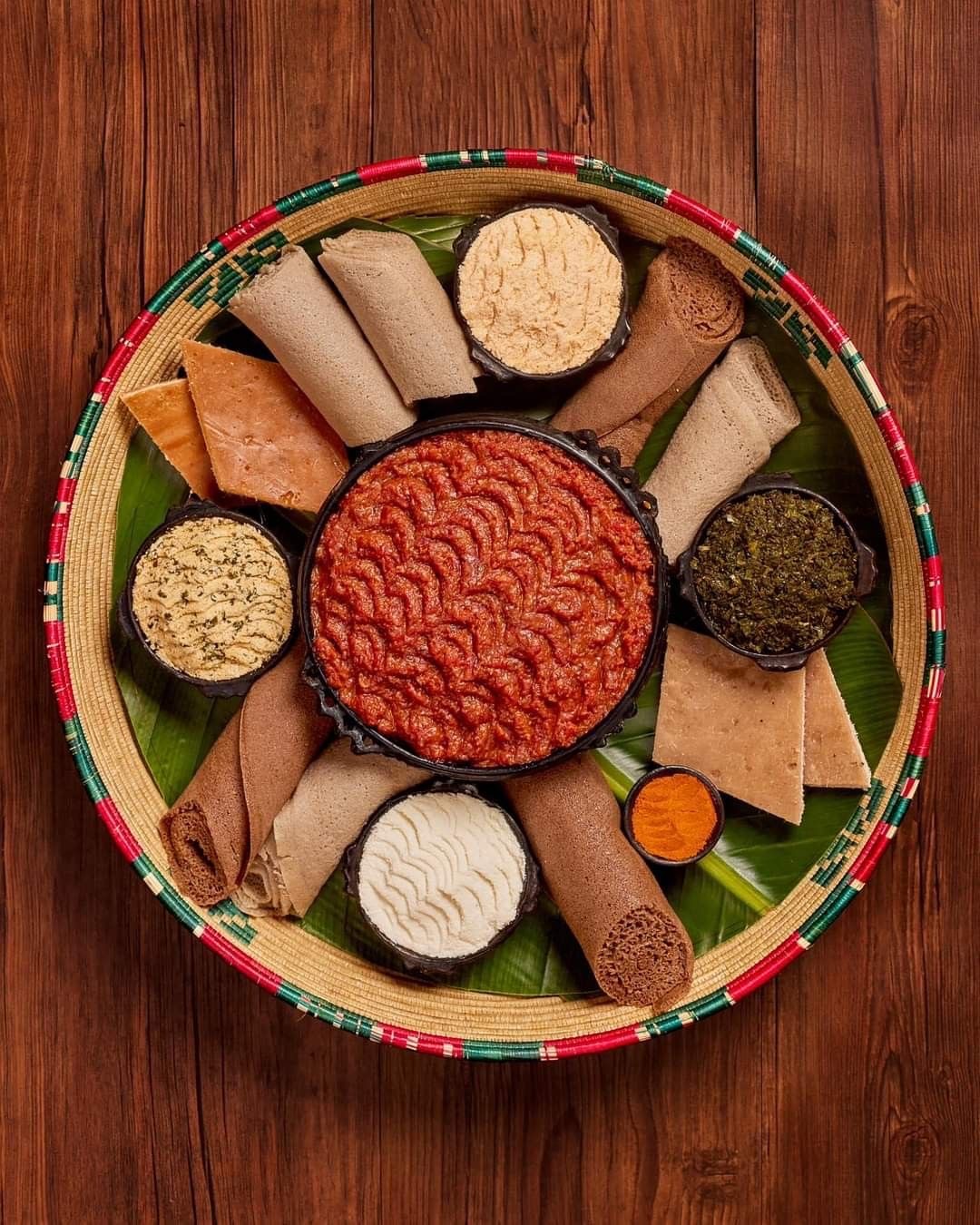 Traditional Ethiopian platter in a woven basket with injera rolls, berbere and spiced sides at Murtesa in Eastleigh, Nairobi