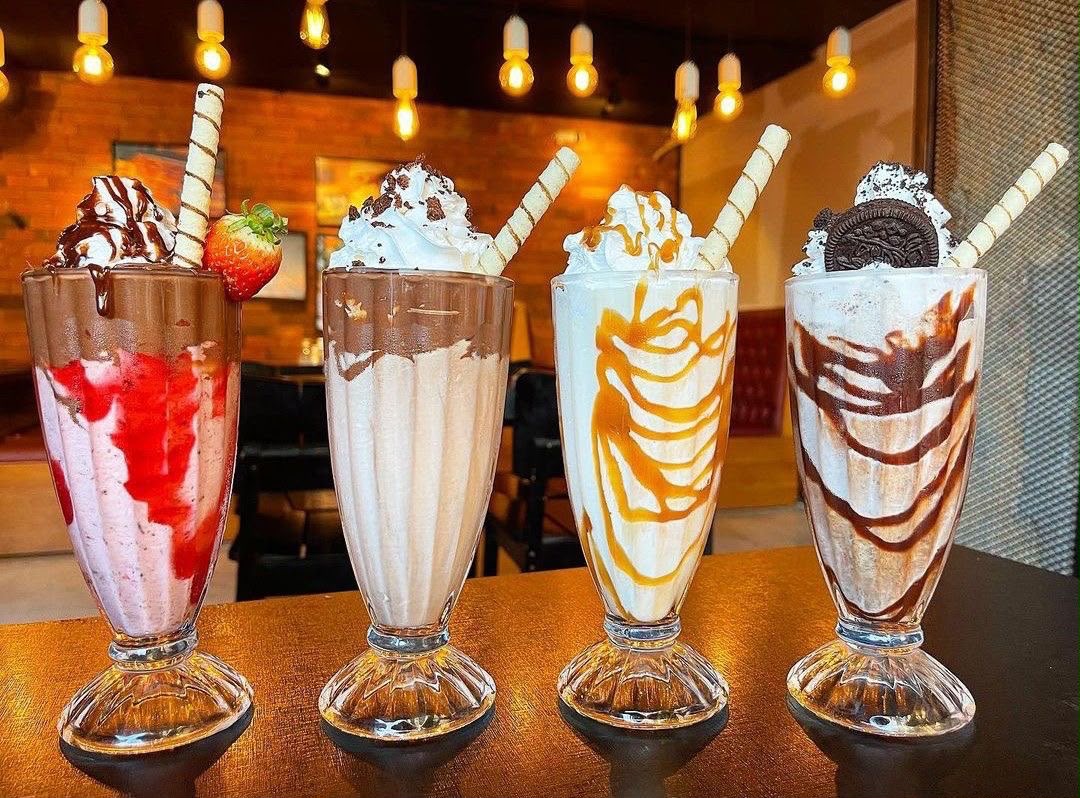 Four tall milkshakes topped with whipped cream, wafer rolls and an Oreo cookie