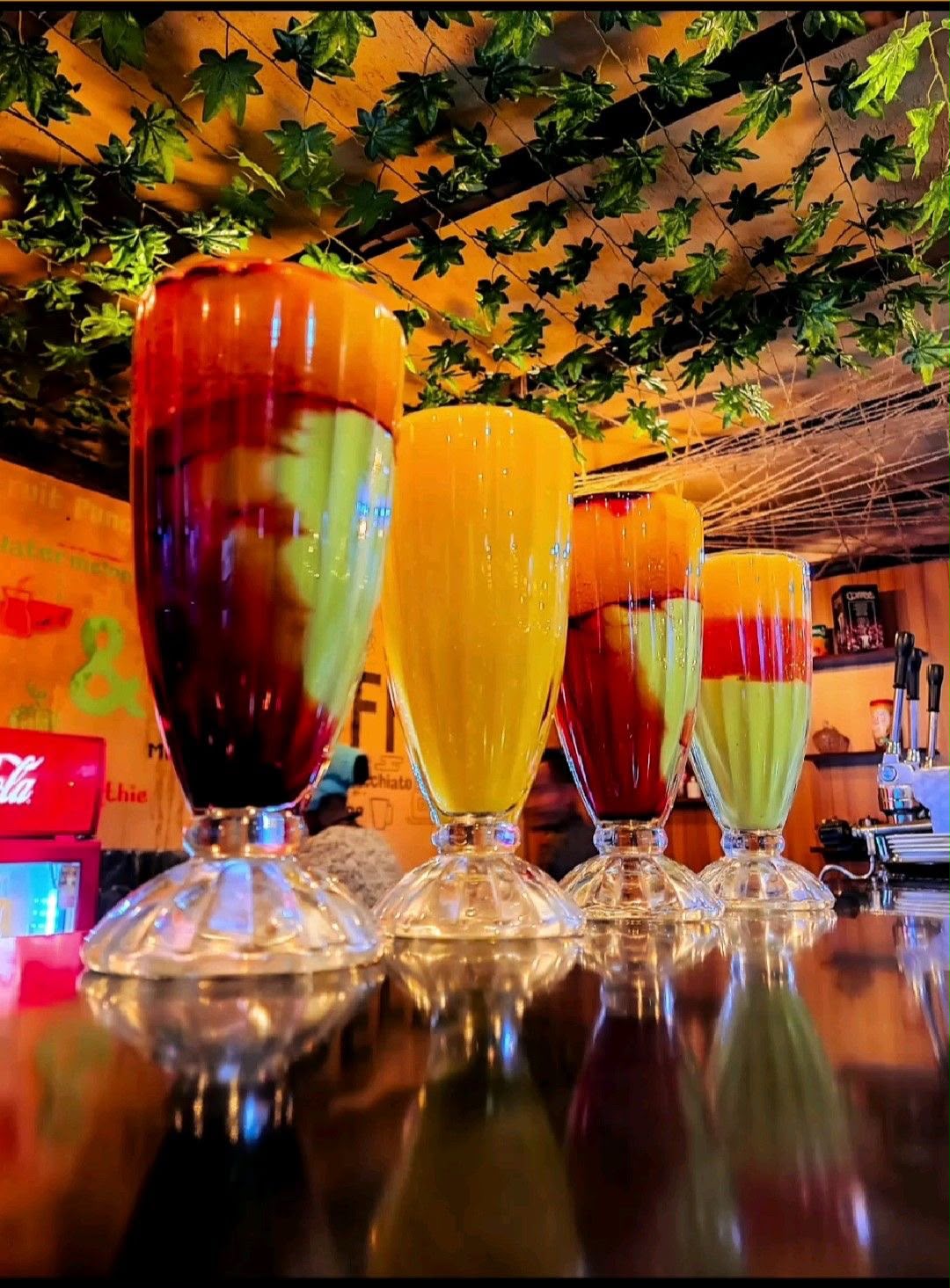 Tall glasses of layered avocado, mango and berry spris juice on a bar counter