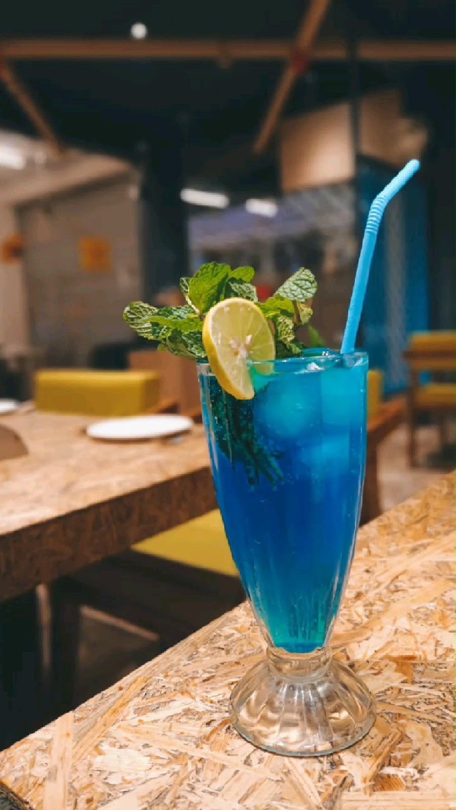 Tall glass of blue mint mojito with lemon slice, mint leaves and a straw